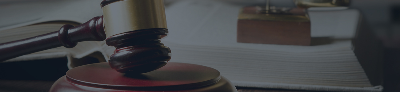 A wooden gavel with an open book and scales of justice in the background on a desk